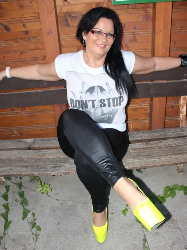 Femme aux cheveux noirs portant un t-shirt blanc, des leggings noirs et des chaussures jaunes fluo, assise sur un banc en bois extérieur.