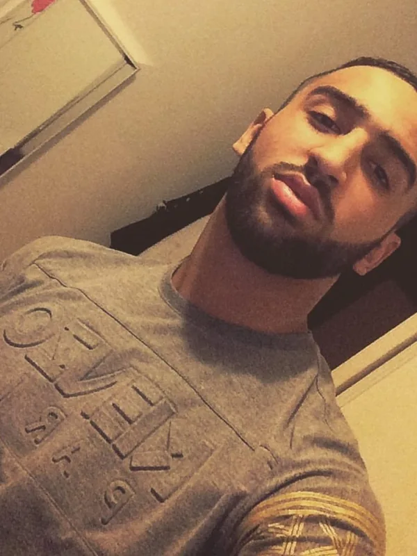 Portrait d'un homme barbu en t-shirt gris prenant un selfie dans un cadre intérieur.