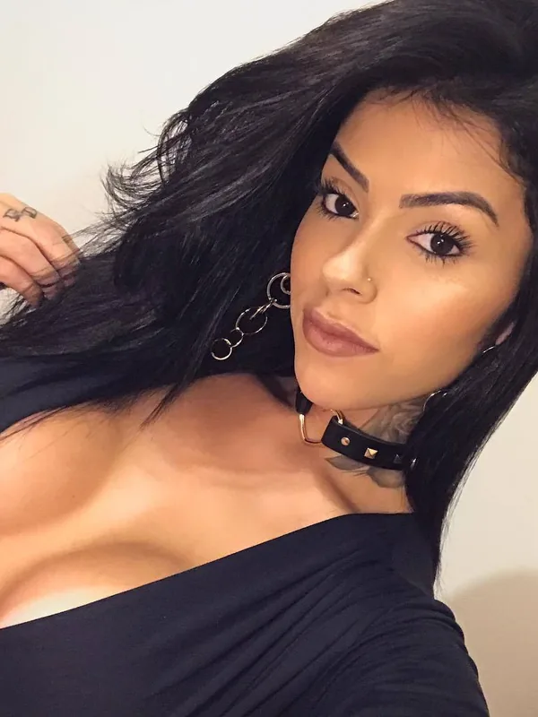 Portrait d'une femme aux cheveux noirs portant un haut noir décolleté et un collier en cuir, regardant l'objectif.