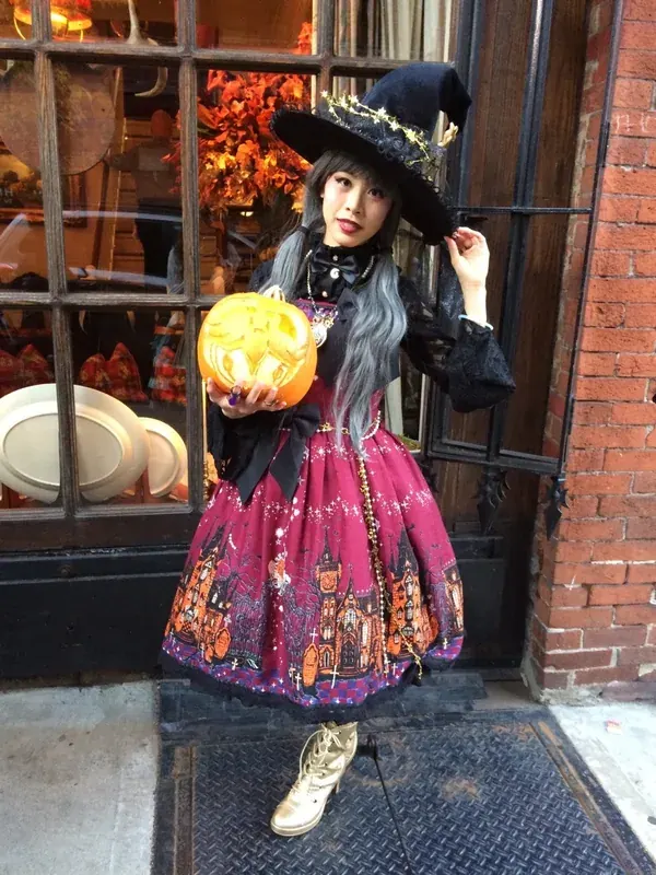 Jeune femme en costume de sorcière tenant une citrouille lumineuse devant une vitrine décorée pour Halloween.