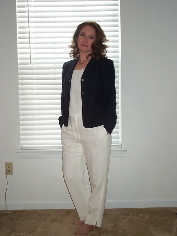 Femme en tenue formelle debout devant une fenêtre aux volets blancs