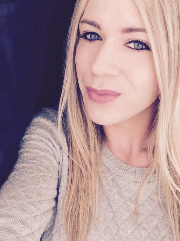 Portrait en gros plan d'une femme aux cheveux blonds et yeux bleus, portant un pull gris, regardant l'objectif.