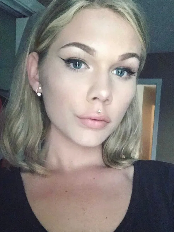 Portrait en plan rapproché d'une femme aux cheveux blonds et yeux bleus, regardant l'objectif, portant un haut noir et un piercing au nez.
