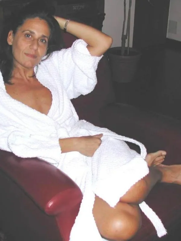 Femme assise sur un fauteuil en cuir rouge, vêtue d'un peignoir blanc, regardant l'objectif.