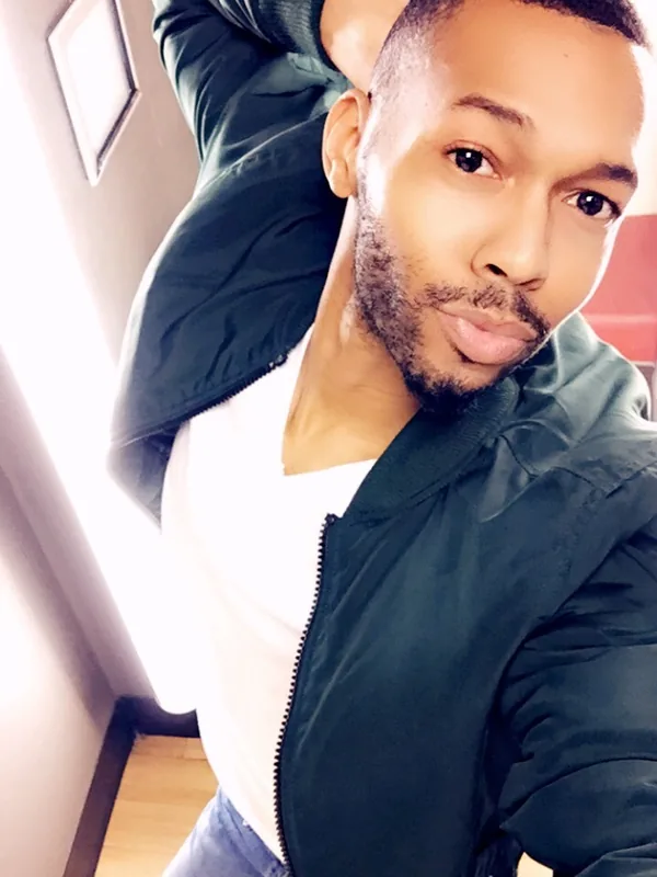 Homme en veste verte et t-shirt blanc prenant un selfie en plongée dans un intérieur lumineux.