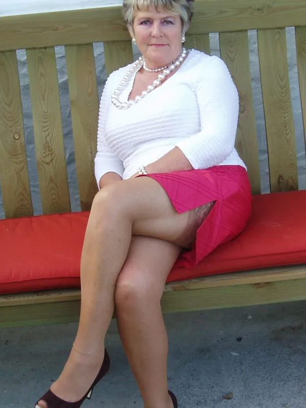 Femme aux cheveux courts blonds assise sur une chaise noire, portant un haut de lingerie noir et blanc, des bas et des sandales à talons.