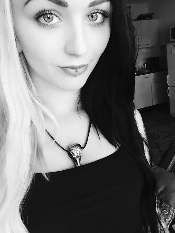Portrait en noir et blanc d'une femme aux cheveux bicolores, regardant l'objectif, portant un haut noir et un collier.