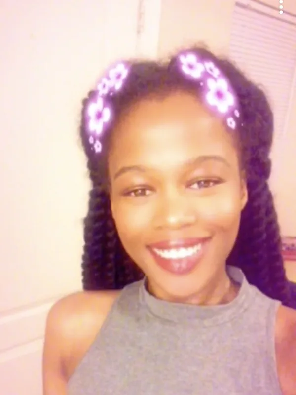 Portrait d'une femme souriante aux cheveux tressés, portant un haut gris, avec un filtre floral lumineux sur la tête.