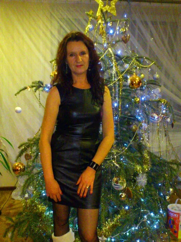Femme en robe noire devant un arbre de Noël décoré avec lumières et ornements.
